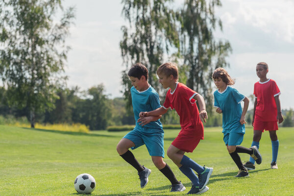 four multicultural kids playing football on grass  