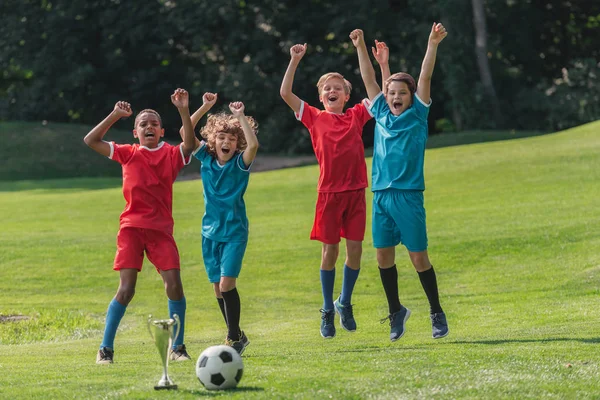 happy multicultural gesturing near trophy and football