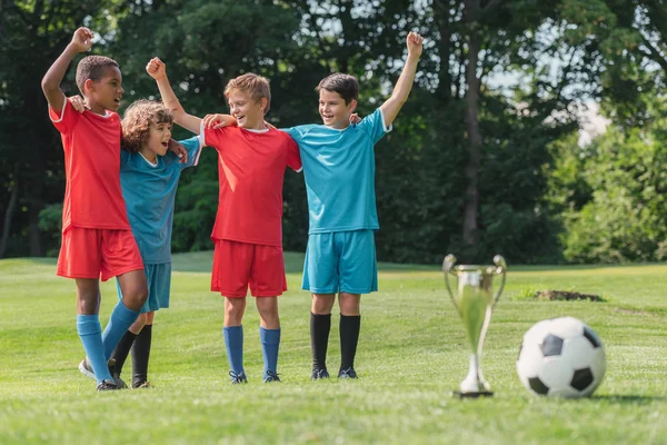 selective focus of multicultural kids gesturing near trophy and football 