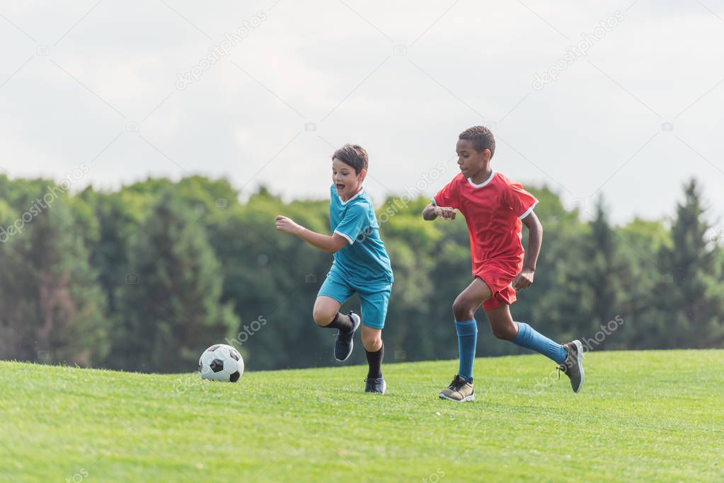 excited multicultural kids playing football on grass 