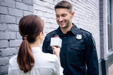 gazeteci mikrofon tutan ve üniformalı yakışıklı polis ile konuşurken