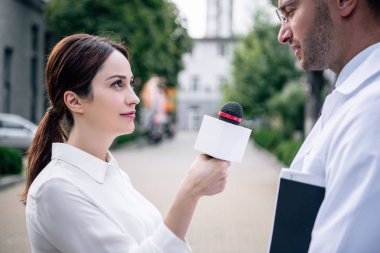 journalist holding microphone and talking with handsome doctor in white coat clipart