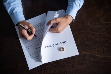 partial view of man sitting at table and signing divorce documents clipart