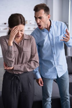 aggressive man in shirt screaming at scared wife at home clipart