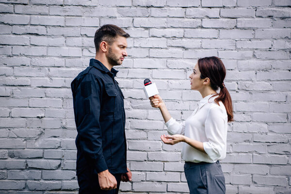 journalist holding microphone and talking with handsome policeman in uniform