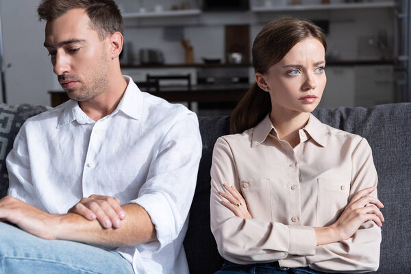 pensive sad man and woman sitting on sofa with crossed arms