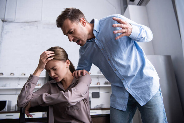 aggressive man in shirt screaming at scared wife at home