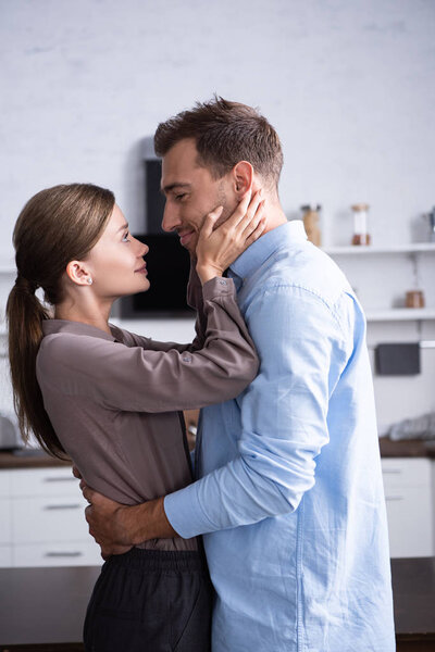 side view of wife and husband embracing in kitchen at home