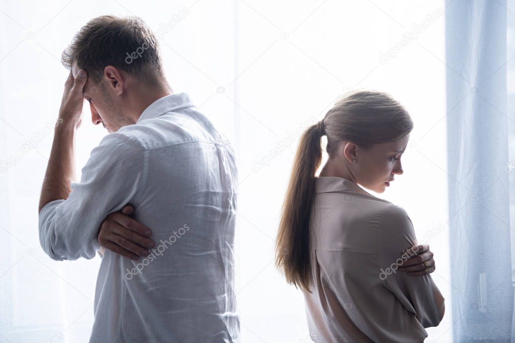 upset woman and man in shirts standing near window