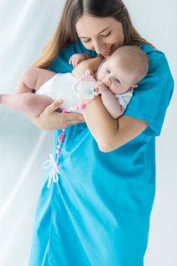 hastanede oyuncak ile çocuğunu tutan çekici ve gülümseyen anne 