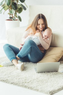çekici anne çocuğunu tutarak ve dairede dizüstü bilgisayar bakarak 