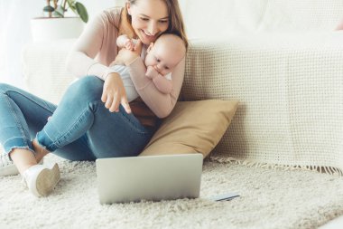 çekici anne çocuğunu tutarak ve dairede dizüstü bilgisayar parmak ile işaret 