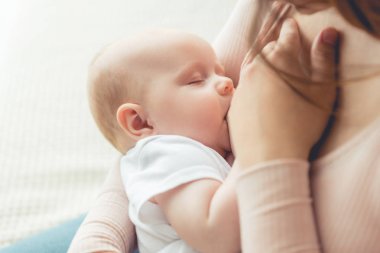 cropped view of mother breastfeeding her child in apartment  clipart
