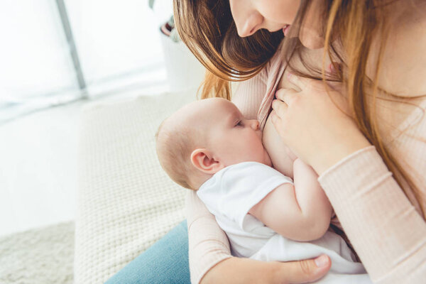 cropped view of mother breastfeeding her child in apartment 