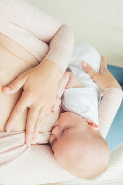 cropped view of mother breastfeeding her child in apartment 