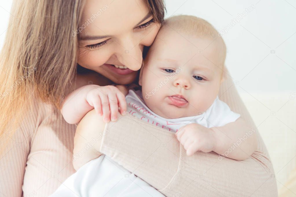 attractive and smiling mother holding her child in apartment 