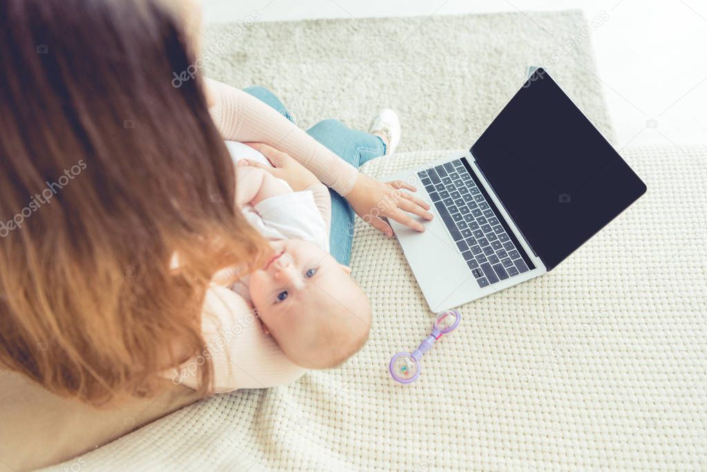 cropped view of mother holding her child and using laptop in apartment 