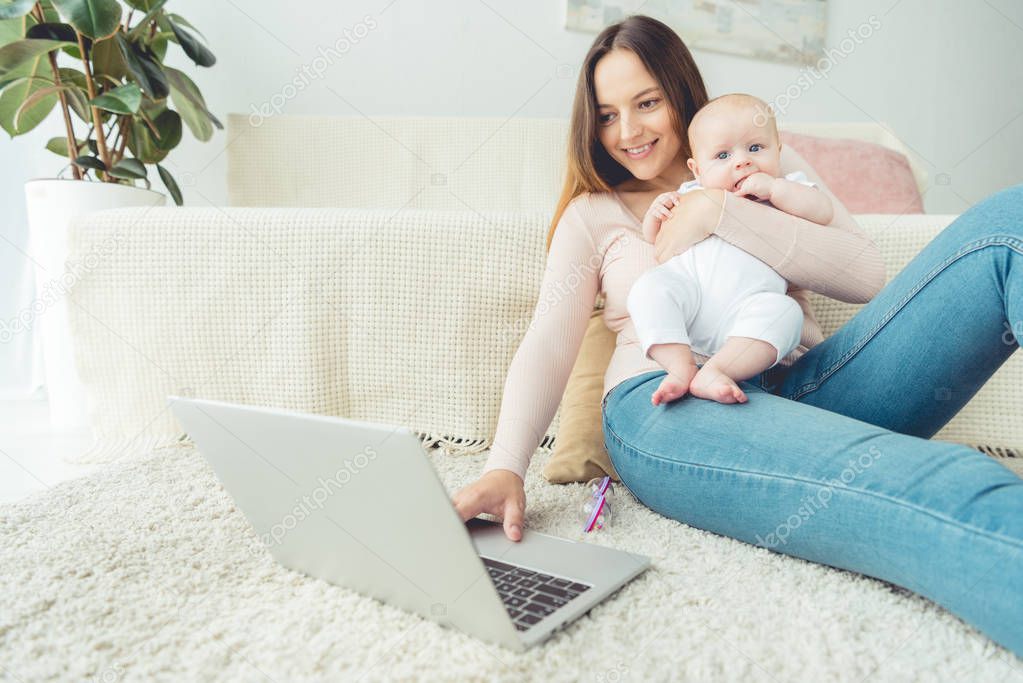 attractive mother holding her child and using laptop in apartment 