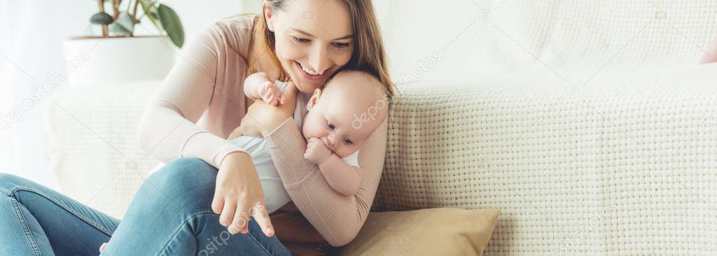 panoramic shot of attractive mother holding her child and pointing with finger in apartment 