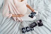 částečný pohled na těhotnou ženu, která sedí na posteli s ultrazvukovém obrázkem