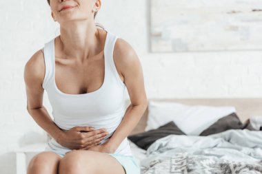 yatakta oturan ve karnına dokunan genç kadının kısmi görünümü