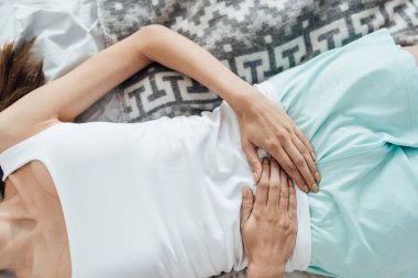 partial view of young woman lying on bed and touching belly clipart