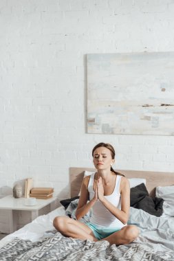 üzgün genç kadın kapalı gözlerle yatakta oturan ve jest lütfen gösteren