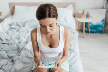 genç kadın yatakta oturan ve gebelik testi tutan
