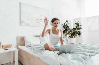 genç kadın kulaklık müzik dinleme ve yatakta dizüstü bilgisayar kullanma