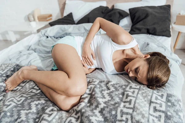 心烦意乱的年轻女子躺在床上 触摸腹部 — 图库照片