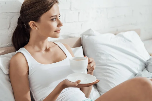 Νεαρή Γυναίκα Ξαπλωμένο Στο Κρεβάτι Και Κρατώντας Ένα Φλιτζάνι Καφέ — Φωτογραφία Αρχείου