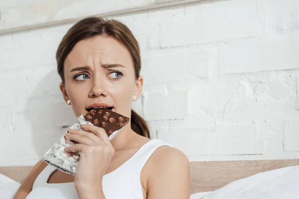 ベッドでナッツとチョコレートを食べる心配した若い女性 — ストック写真