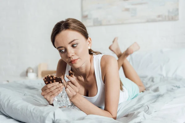 沉思赤脚年轻女子拿着巧克力与坚果在床上 — 图库照片