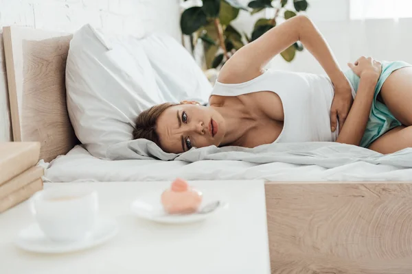 Mulher Sofrendo Deitado Cama Tocando Barriga Olhando Para Cupcake — Fotografia de Stock