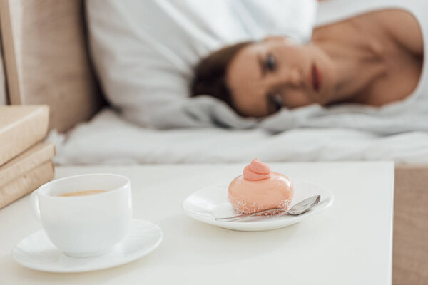selective focus of suffering woman lying in bed and looking at cupcake