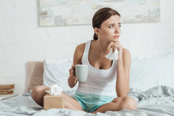 紧张的年轻女子坐在床上 拿着一杯茶 — 图库照片