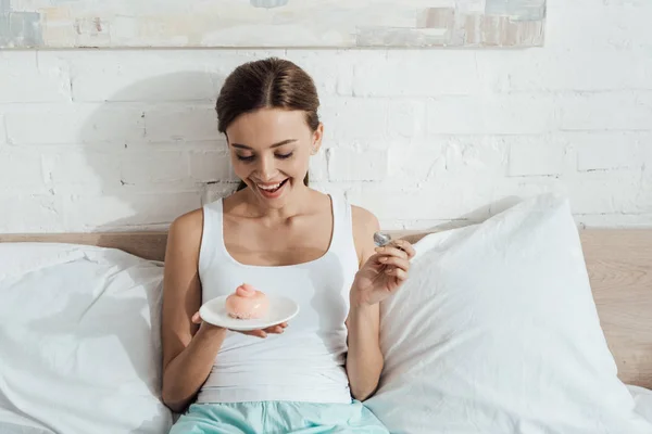 Cheerful Young Woman Lying Bed Eating Cupcake — Stock Photo, Image