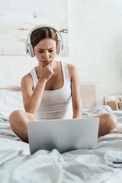 Fundersam Ung Kvinna Lyssnar Musik Hörlurar Och Använda Laptop Sängen — Stockfoto