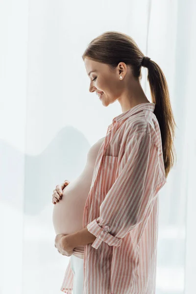 Widok Boku Szczęśliwej Kobiety Ciąży Uśmiechnięty Dotykając Brzuch — Zdjęcie stockowe