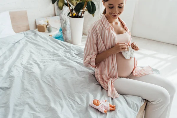 Sorrindo Mulher Grávida Sentada Cama Segurando Sapatos Bebê — Fotografia de Stock