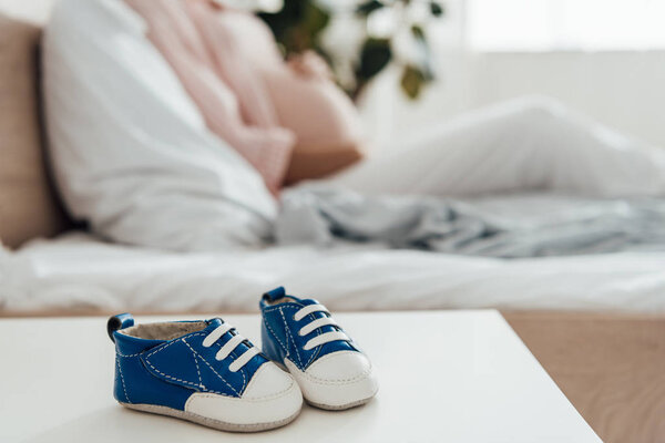 selective focus of pregnant woman and baby shoes on foreground