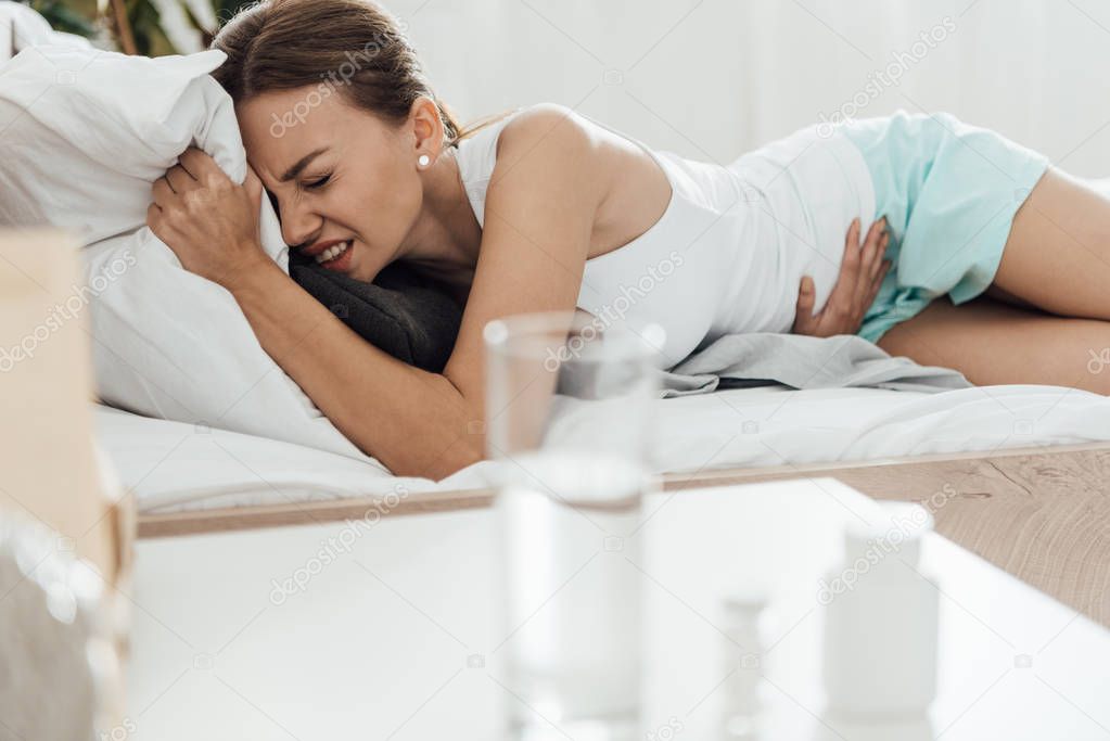 suffering woman in bed and pills with glass of water on foreground