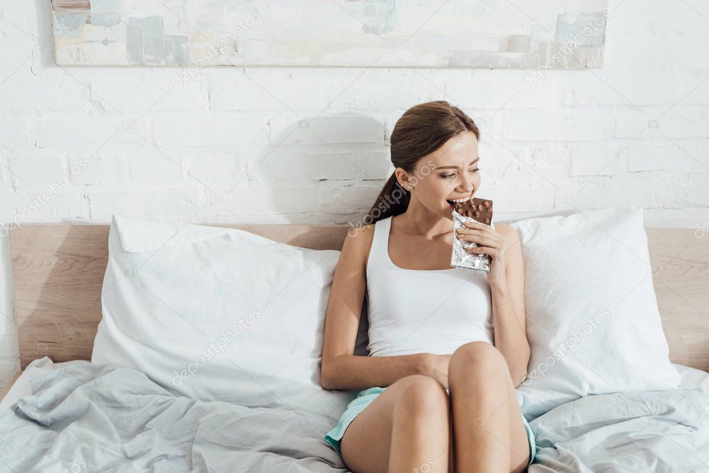 young woman eating chocolate with nuts in bed