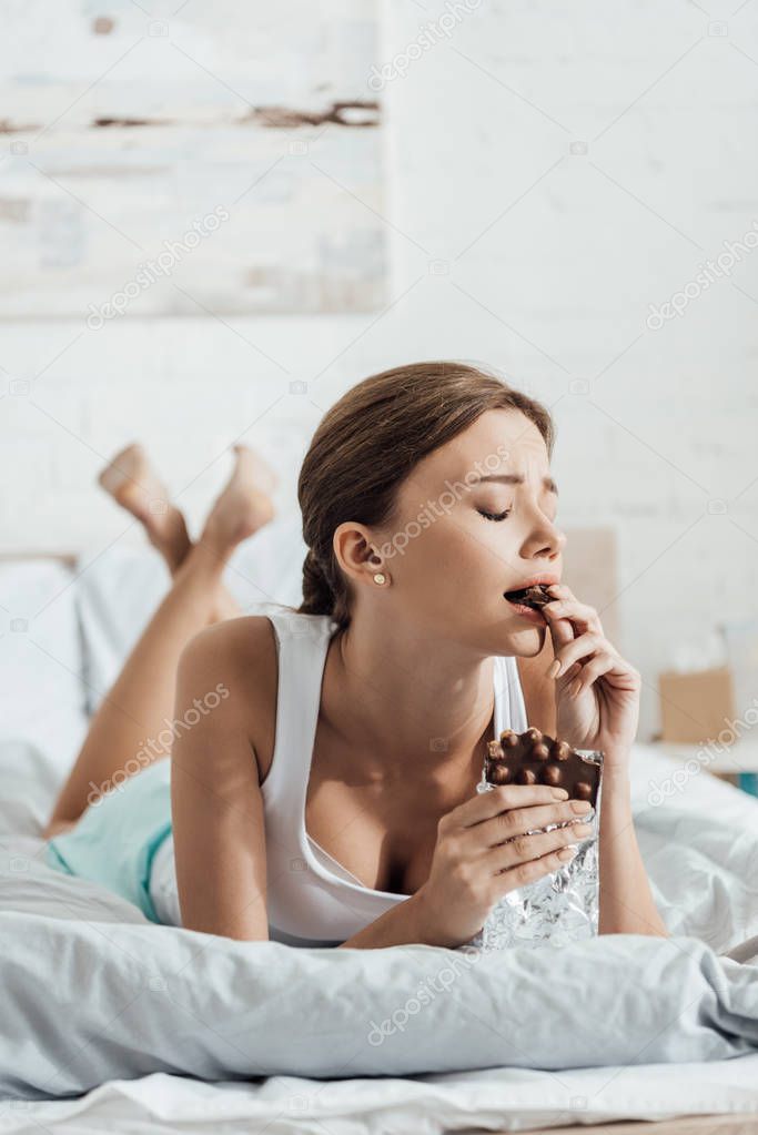 barefoot young woman eating chocolate with nuts in bed