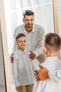 ayna önünde duran beyaz gömlekli gülümseyen baba ve oğul