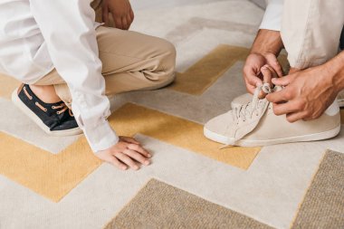partial view of father teaching son to tying shoelaces at home clipart