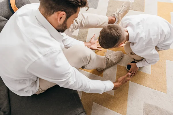 overhead view of father teaching son to tying shoelaces at home