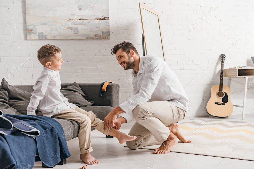 smiling father helping son to get dressed at home