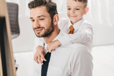 cheerful boy embracing bearded dad in white shirt at home clipart