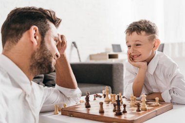 dad and son playing chess together at home clipart